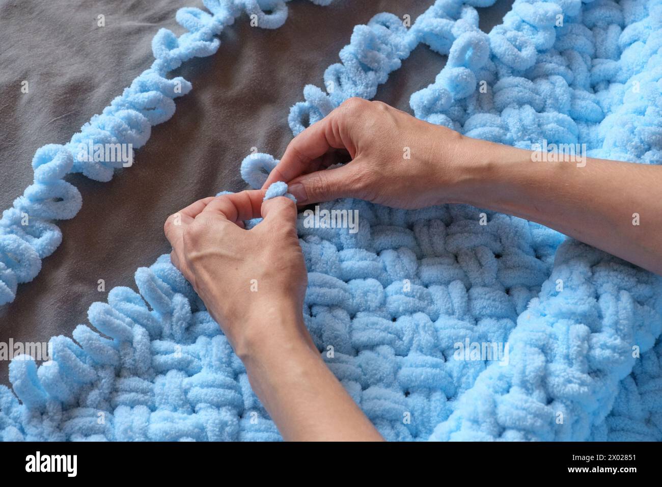 Une femme fabrique avec amour une couverture bleue pour son petit-fils de ses propres mains, chaque point témoignant de son soin et de son dévouement. Créez des souvenirs précieux Banque D'Images