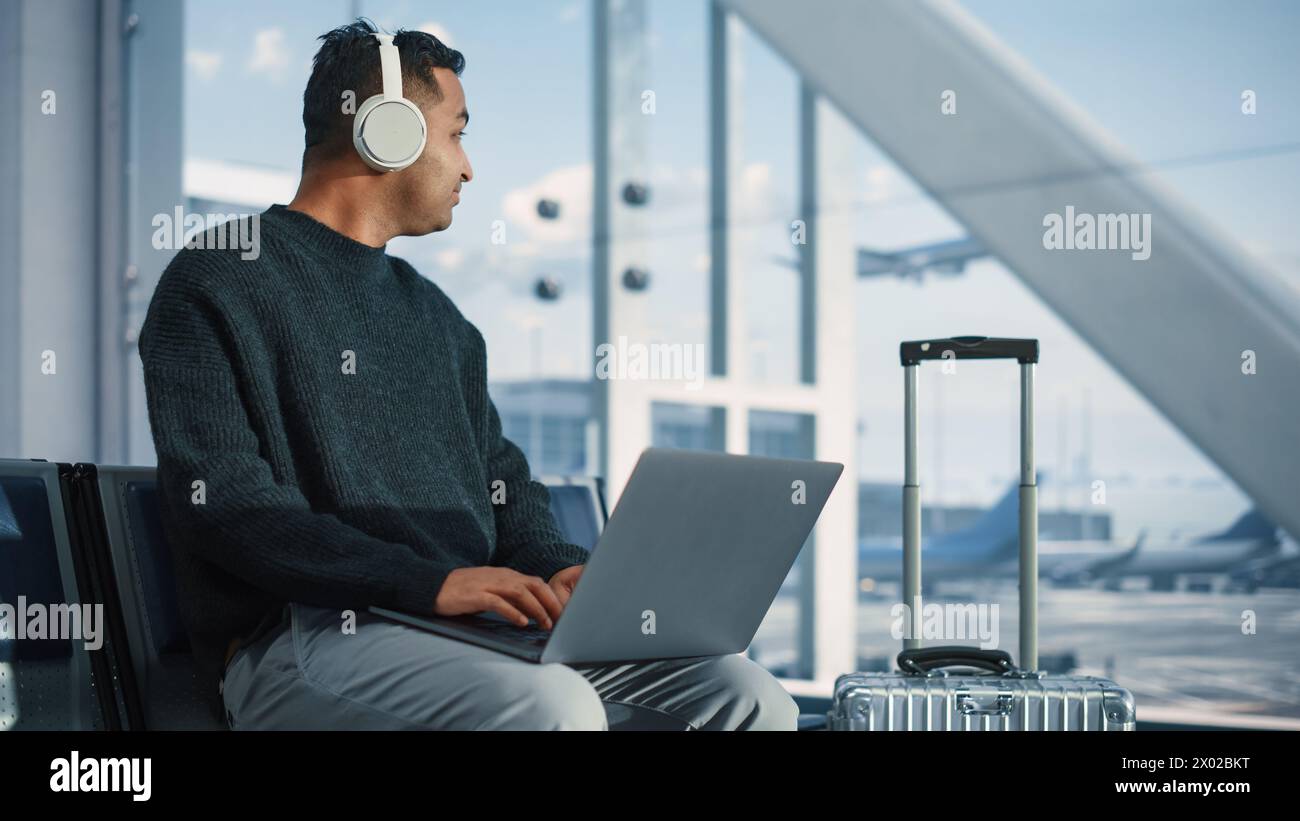 Terminal de l'aéroport : homme d'affaires utilise un ordinateur portable, écoute des musiques ou Podcast dans casque, en attente de vol. Voyageur Digital entrepreneur travailler à distance en ligne dans le salon d'embarquement de Airline Hub Banque D'Images