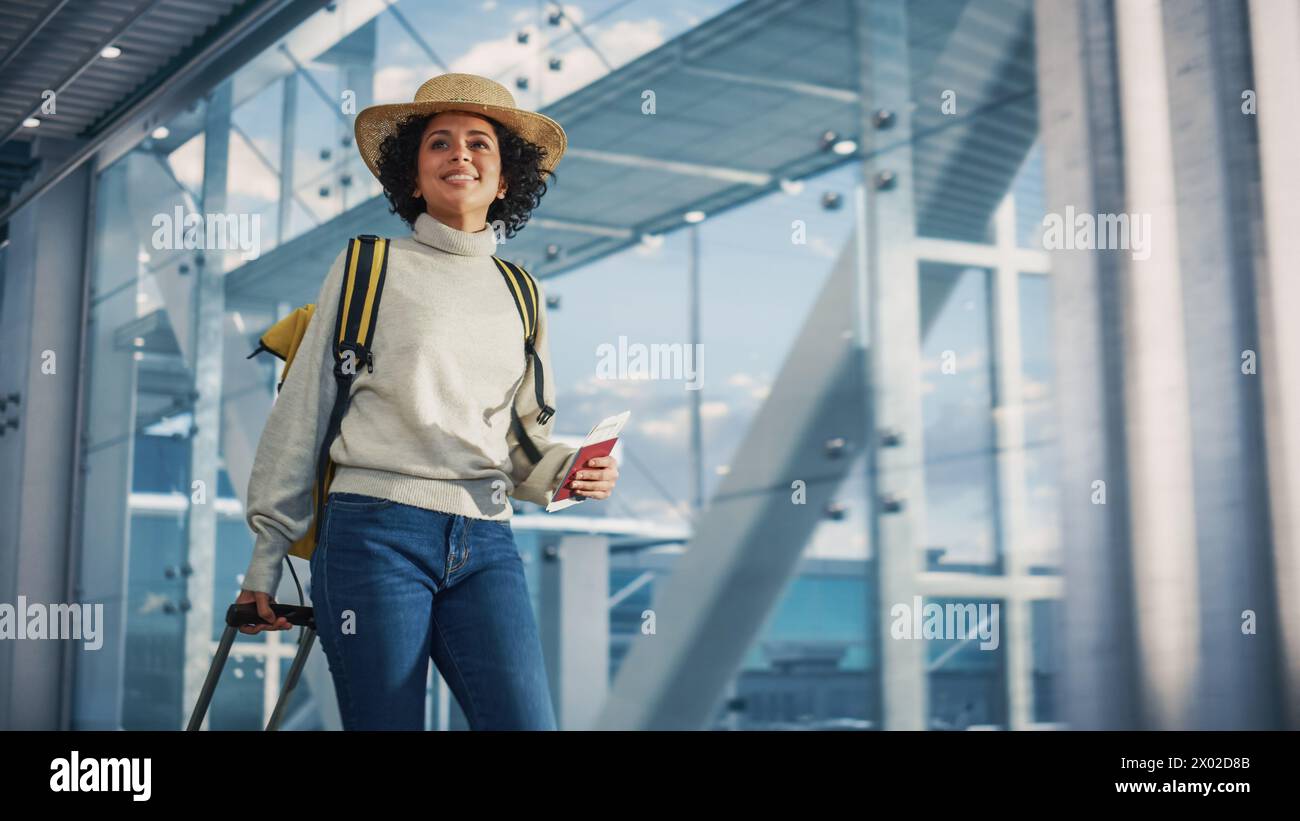 Terminal de l'aéroport : belle femme noire souriante tient un billet, traverse dans Airline Hub jusqu'aux portes où l'avion attend. Happy African American Female est prêt pour le vol vers la destination de vacances Banque D'Images