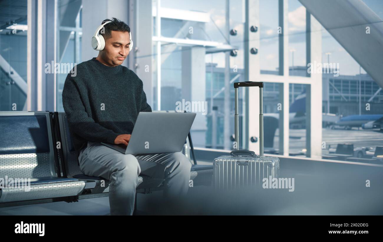 Terminal de l'aéroport : homme d'affaires utilise un ordinateur portable, écoute des musiques ou Podcast dans casque, en attente de vol. Voyageur Digital entrepreneur travailler à distance en ligne dans le salon d'embarquement de Airline Hub Banque D'Images