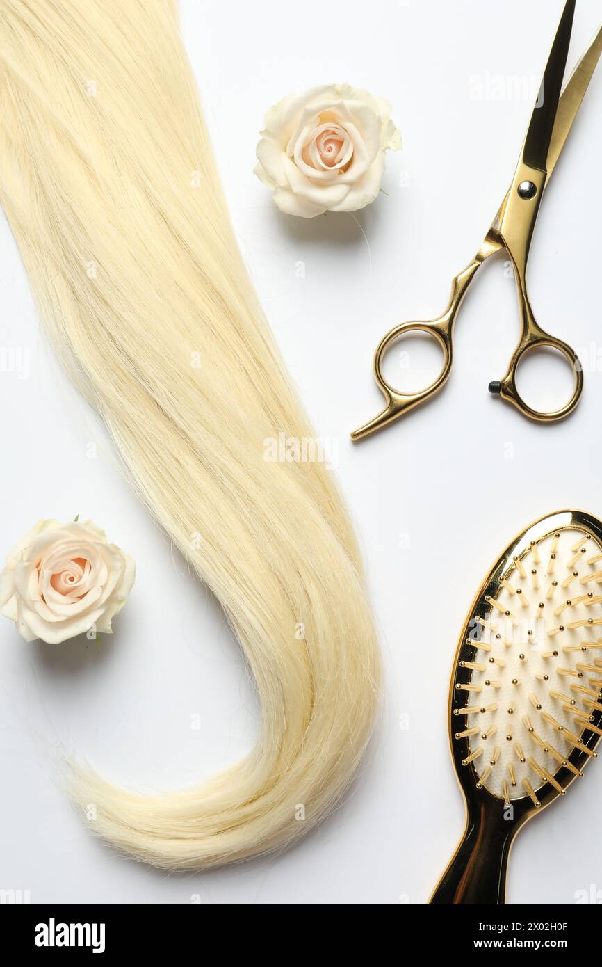 Outils de coiffure. Mèche de cheveux blonds, ciseaux, brosse et fleurs sur sac à dos blanc, pose à plat Banque D'Images