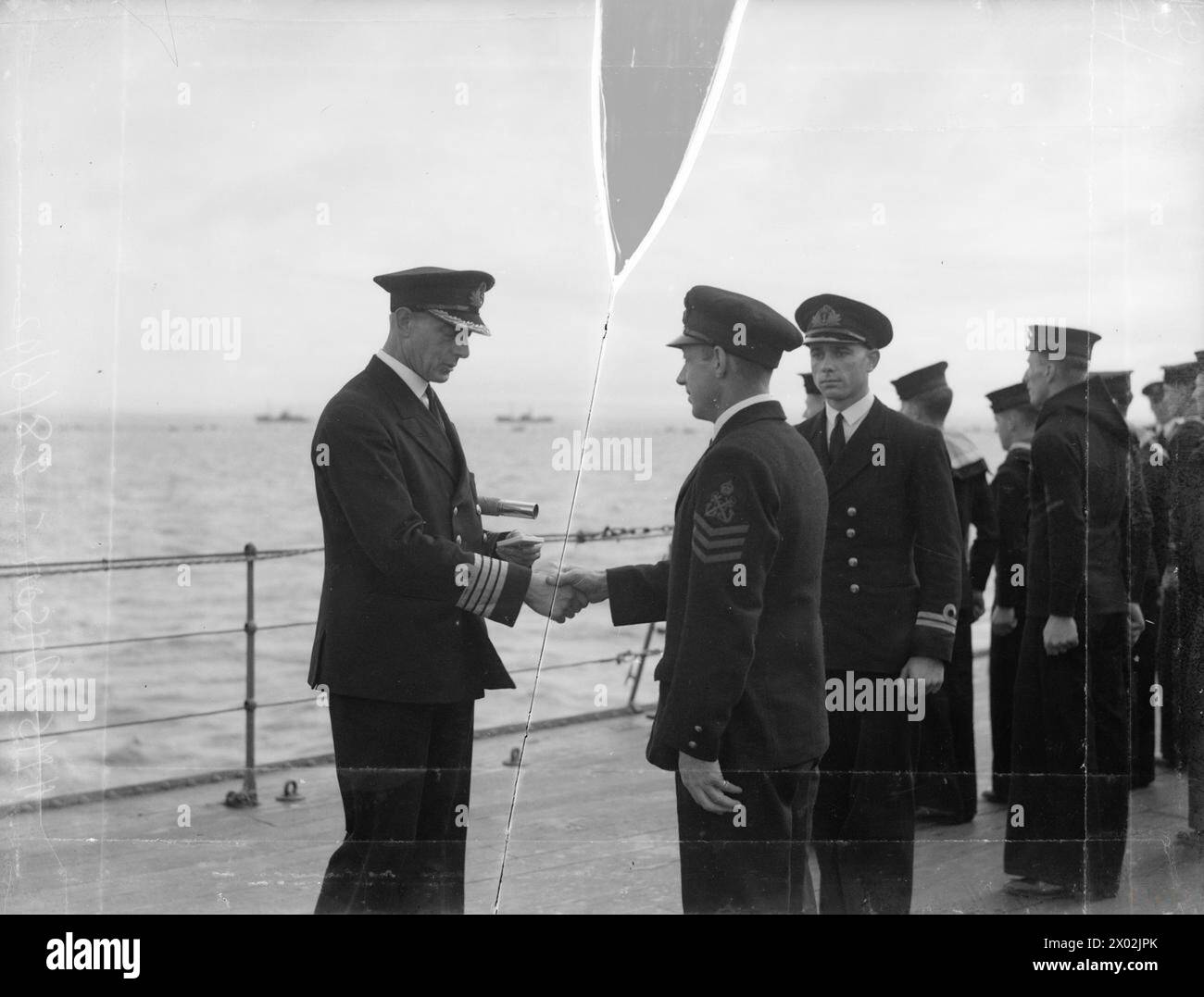 LE HMS ANSON DÉTIENT DES DIVISIONS AU MOUILLAGE DE LA FLOTTE. 28 JUIN 1942. - Le Capt H R G Kinaham, CBE, RN, le capitaine de l'Anson, félicitant un maître Stoker de lui avoir remis une médaille de longue durée et de bonne conduite Banque D'Images