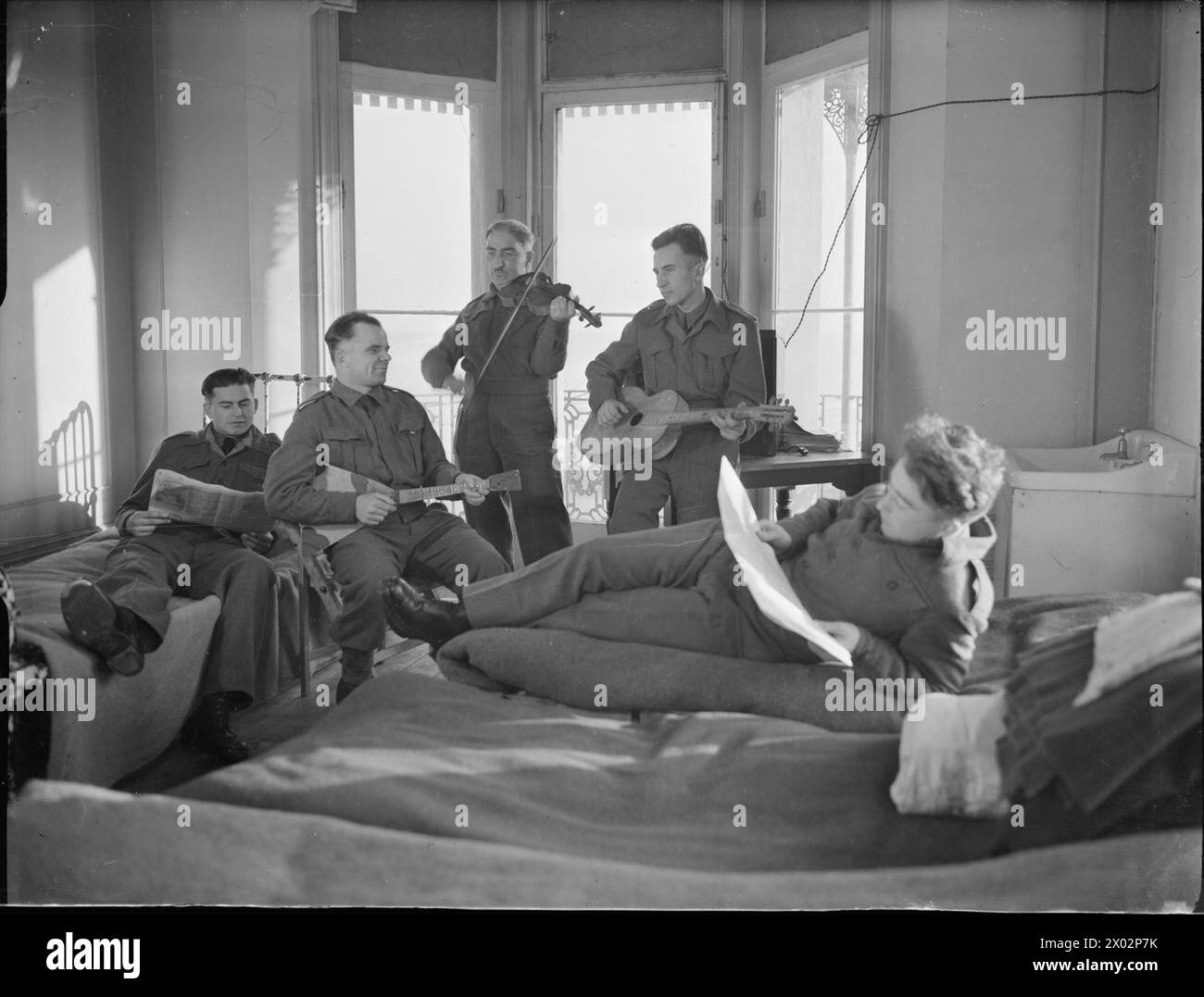 PRISONNIERS RUSSES LIBÉRÉS EN ANGLETERRE : LA VIE QUOTIDIENNE DANS LEUR CAMP DE WORTHING, SUSSEX, ANGLETERRE, Royaume-Uni, 1945 - dans l'un des dortoirs de leur camp à Worthing, un groupe de prisonniers russes libérés s'entraînent sur leurs instruments de musique faits maison, tandis que d'autres lisent les journaux. De gauche à droite, ils sont :le lieutenant junior Maresh (lecture), Aleksei Matveyenko (balalaïka), le soldat Giroriy Zurabov (violon), le lieutenant junior George Kharchenko (guitare) et le lieutenant junior Nagoev (lecture du journal) Banque D'Images