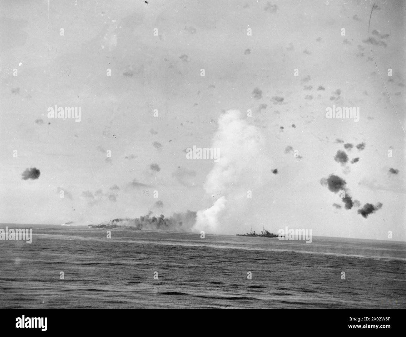Le 12 août 1942, au cours de l'opération Pedestal, le HMS Indomitable est bombardé et prend feu tandis que le HMS Charybdis, un croiseur de classe Dido, inspecte le porte-avions. Banque D'Images