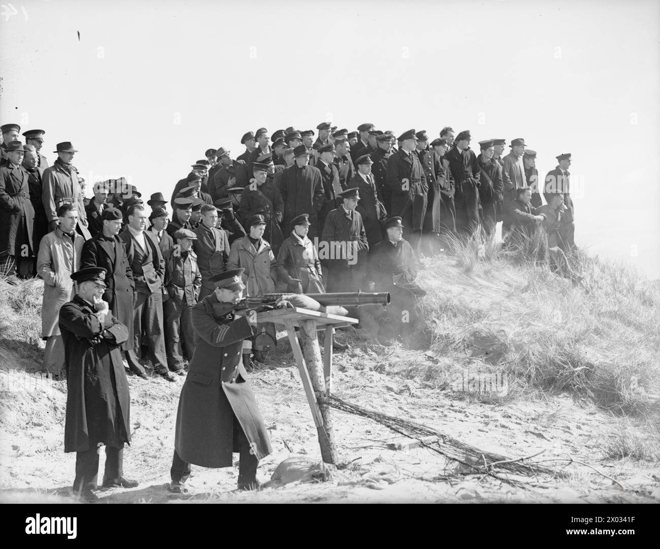 Le 1-2 avril 1942, à Liverpool, des marins marchands fréquentent une école d'artillerie pour observer un tir de démonstration mené par un instructeur de la Royal Marine. Banque D'Images