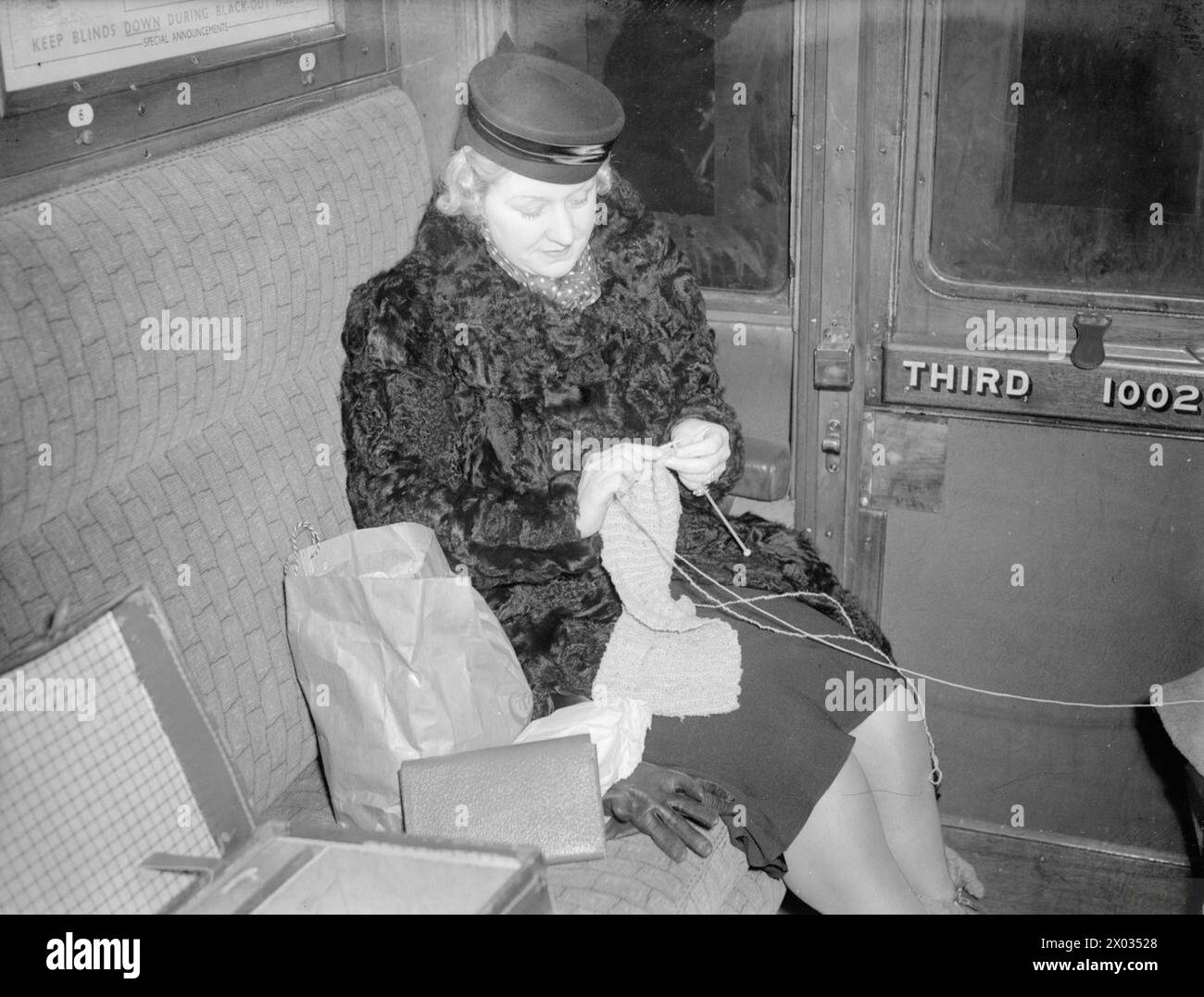 LES CARTER EN TEMPS DE GUERRE : LA VIE QUOTIDIENNE D'Une FAMILLE BRITANNIQUE SUR LE FRONT INTÉRIEUR, ANGLETERRE, C 1940 - Mme carter est assise dans un wagon de chemin de fer et tricote un vêtement pour l'un de ses deux enfants. Elle voyage de London Victoria à Hayward's Heath, Sussex, pour rendre visite à ses enfants, qui ont été évacués là-bas Banque D'Images