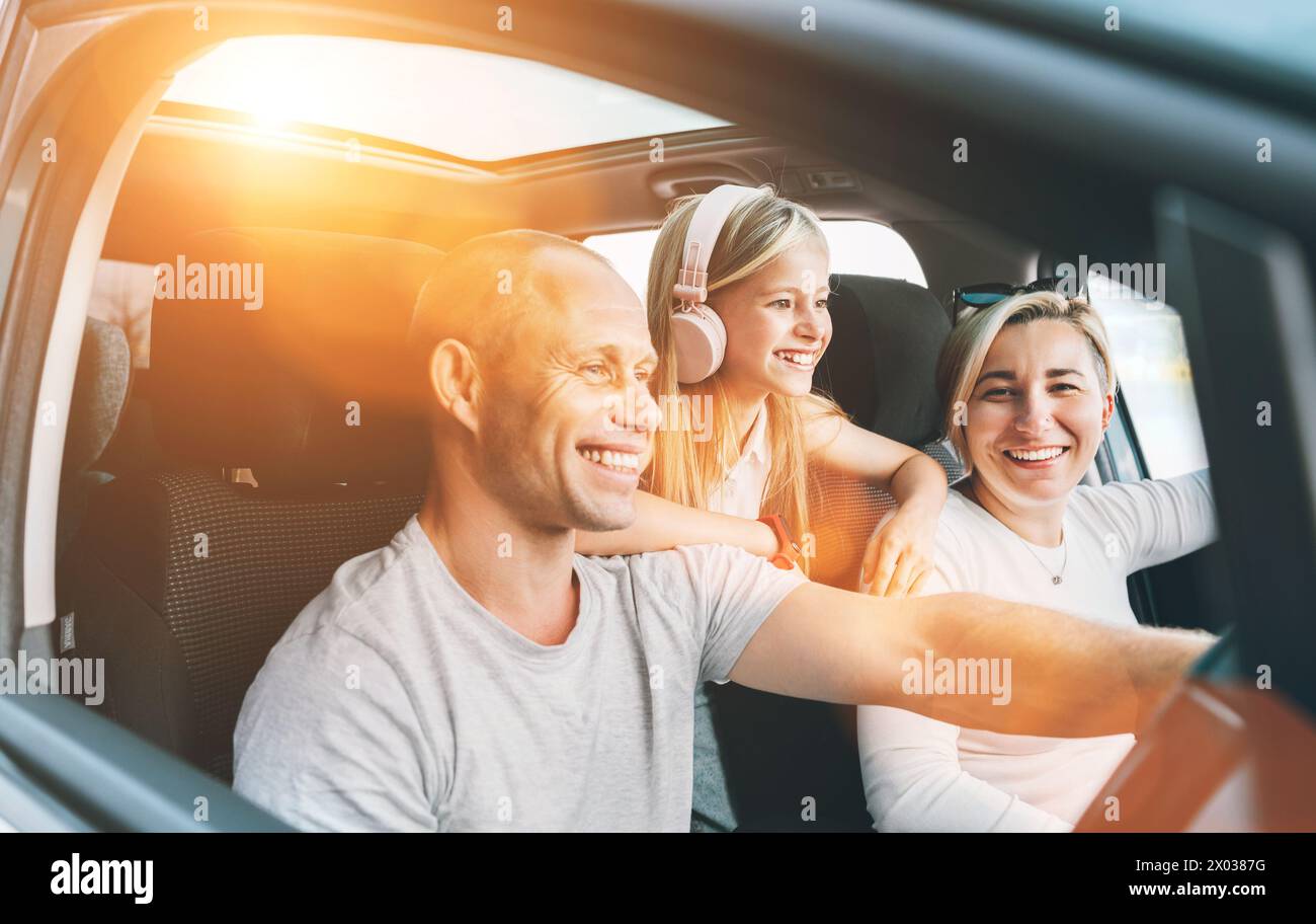 Heureux jeune couple avec fille à l'intérieur de la voiture moderne avec toit panoramique pendant auto trop. Ils sourient, rient pendant le Road trip. Valeur familiale Banque D'Images