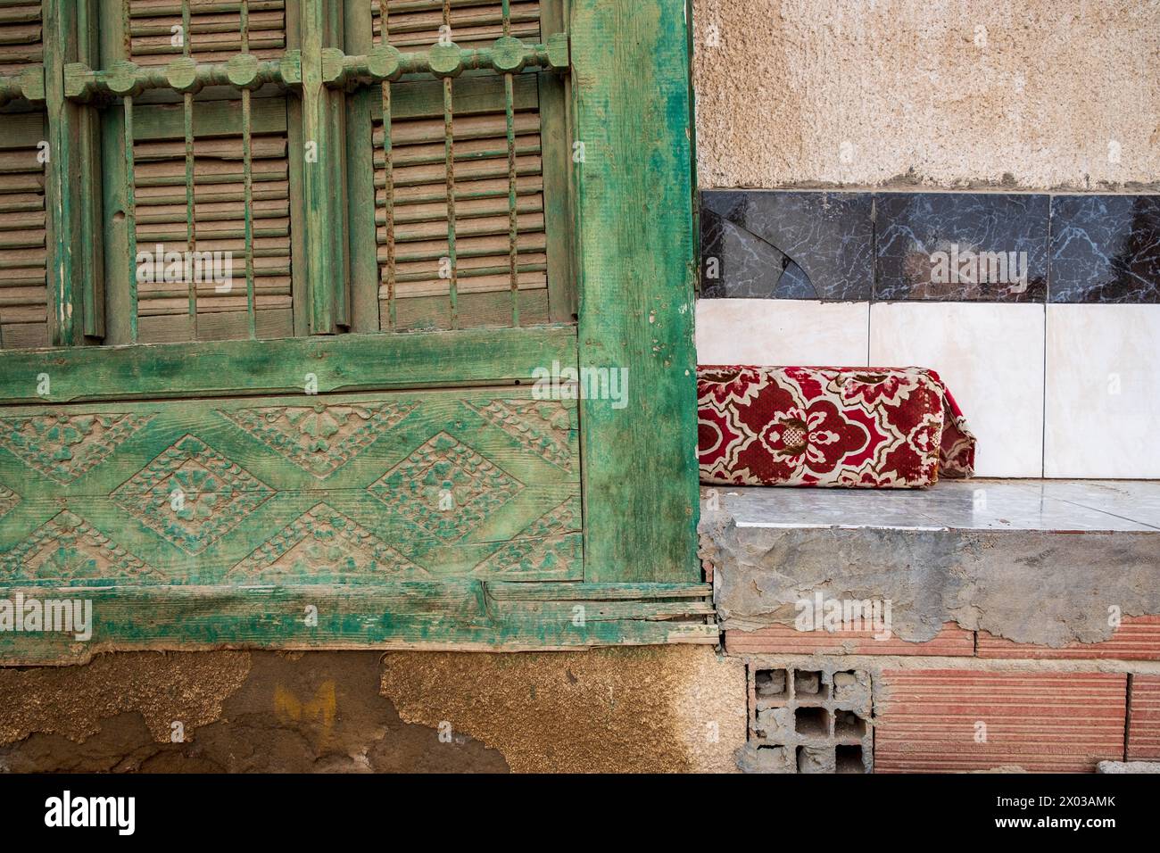 Détail d'un mashrabiya ou couverture traditionnelle d'écran en bois sculpté à côté d'un banc carrelé avec coussin rouge à l'extérieur d'une maison arabe dans le Banque D'Images