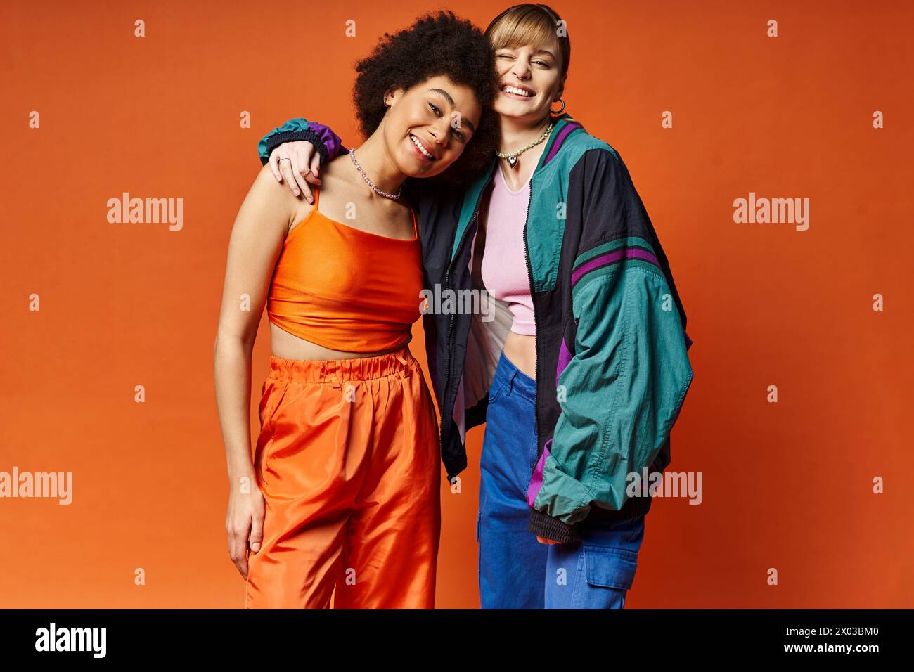 Deux belles femmes de différents horizons culturels debout ensemble dans un studio sur un fond orange. Banque D'Images