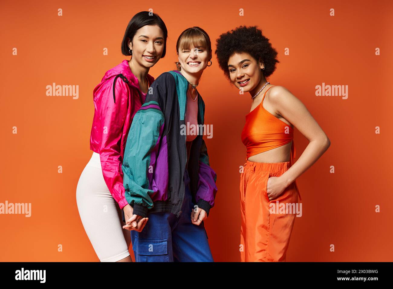 Trois femmes d'ethnies différentes debout ensemble dans un studio sur un fond orange, rayonnant de beauté et d'unité. Banque D'Images