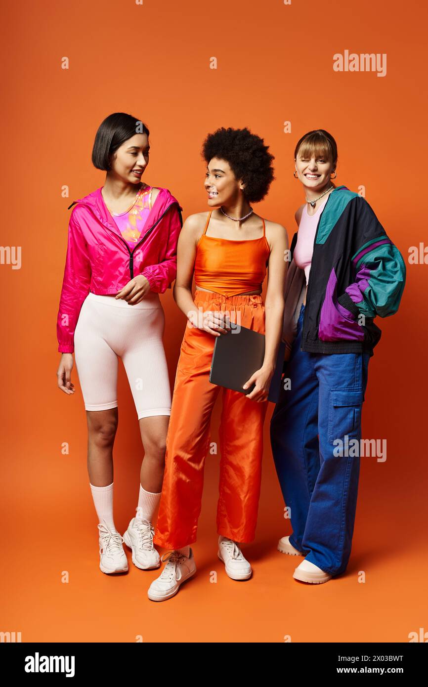 Trois belles femmes de différentes ethnies debout unies devant un fond orange. Banque D'Images