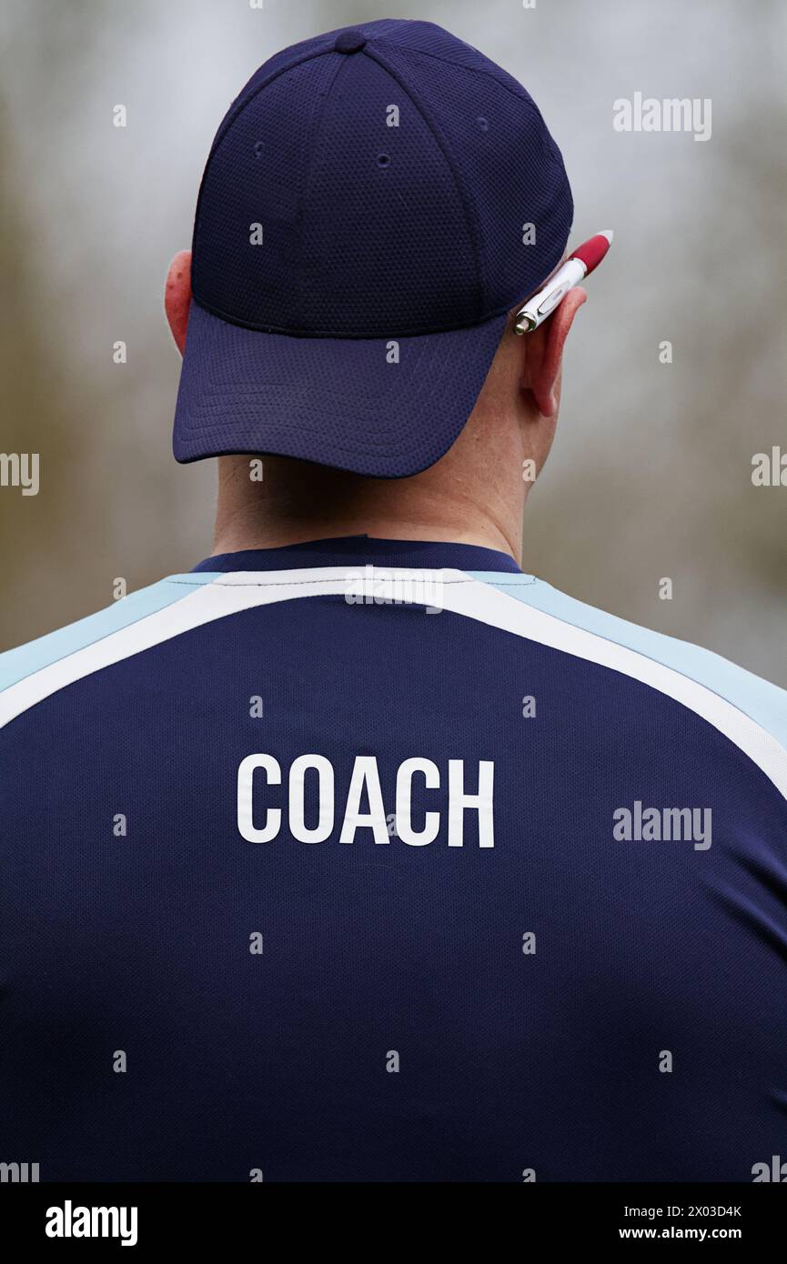 Vue arrière d'Un entraîneur sportif d'équipe masculin, entraîneur avec stylo derrière l'oreille dans casquette de baseball à l'arrière et chemise avec entraîneur dans le texte Banque D'Images