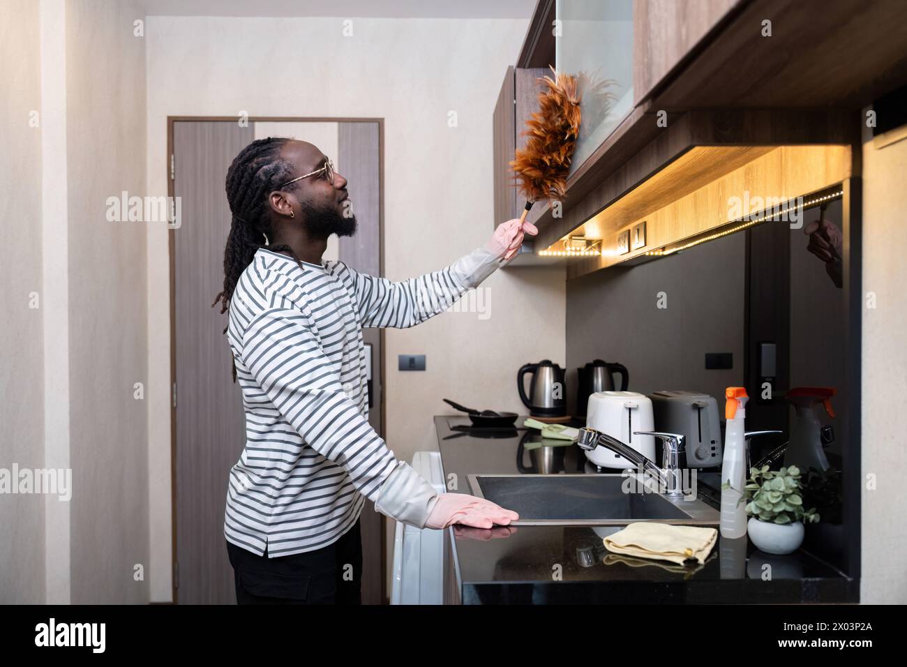 Homme afro-américain jeune utiliser le nettoyage de plumeau dans la cuisine à la maison Banque D'Images