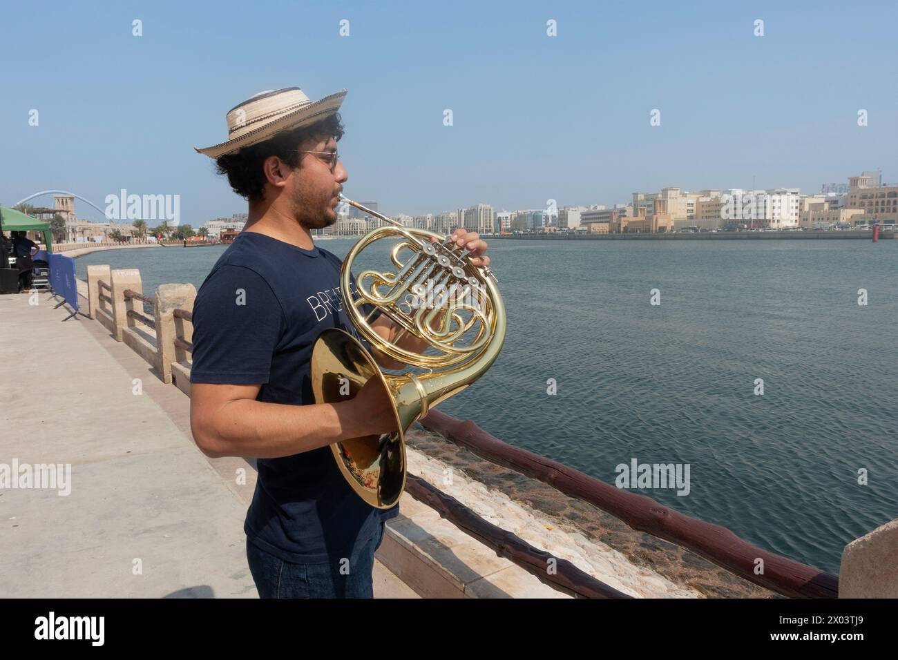 Jeune musicien jouant la corne française sur la rive de la crique dans le quartier historique d'Al Shindagha, Dubaï, Émirats arabes Unis. Banque D'Images