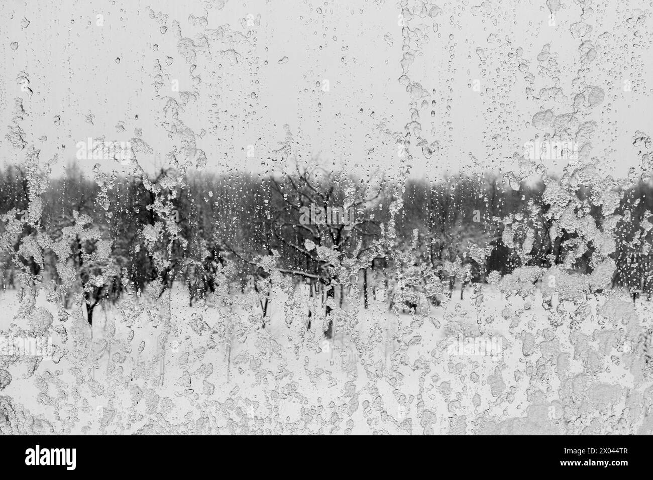 La pluie gelée tombe sur une fenêtre avec une vue floue et enneigée. Glace et eau sur la fenêtre gros plan. Banque D'Images