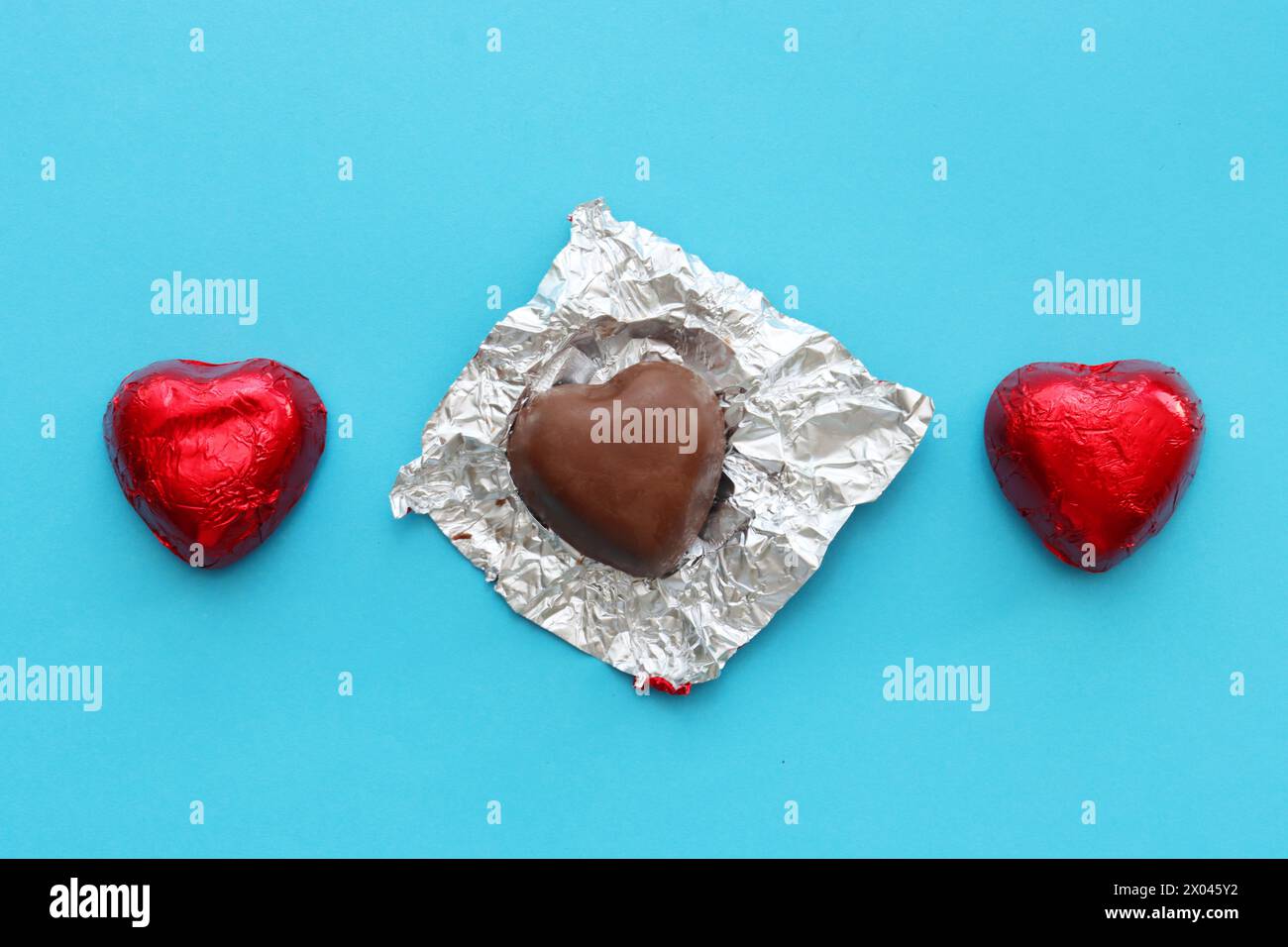 Deux chocolats et un avec un wrapper non emballé.trois cœurs de chocolat sur un fond bleu, vue de dessus. Banque D'Images