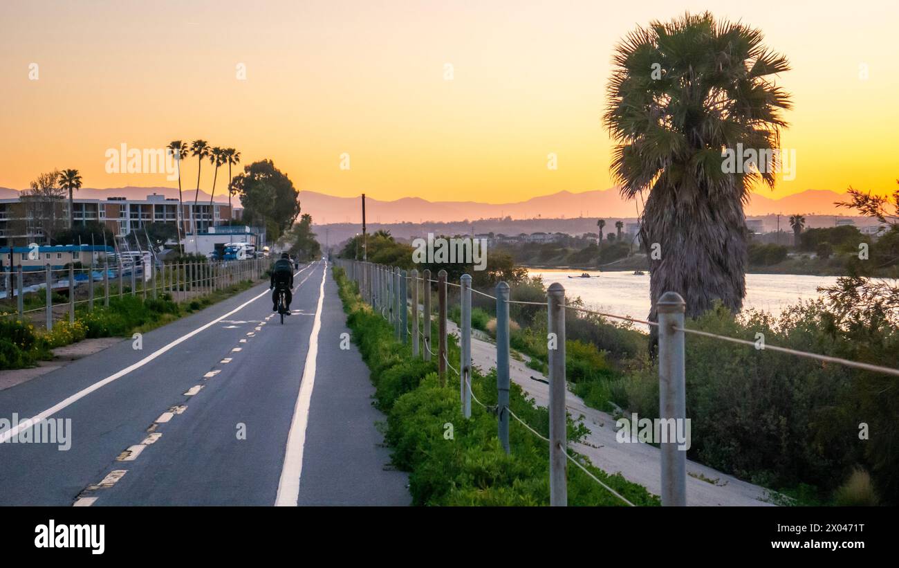 Un homme faisant du vélo sur une piste cyclable près de Marina del Rey, Californie, États-Unis, à l'aube, avec des montagnes brumeuses en arrière-plan et des zones humides à proximité Banque D'Images