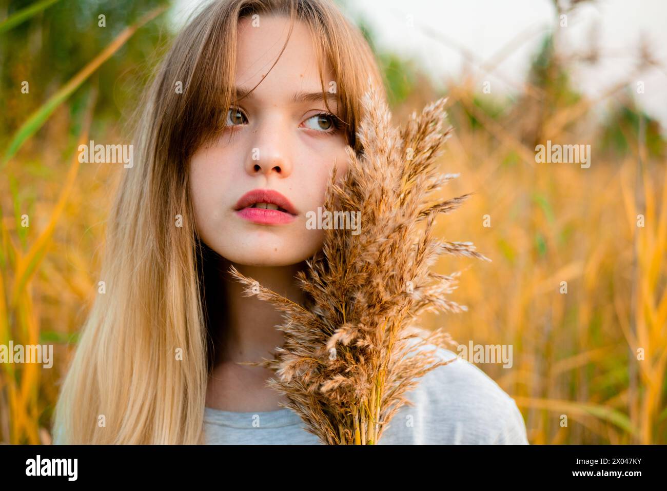 Belle jeune fille portant un t-shirt gris vierge et un Jean noir posant contre l'herbe haute verte et jaune au début de l'automne chaud. Banque D'Images