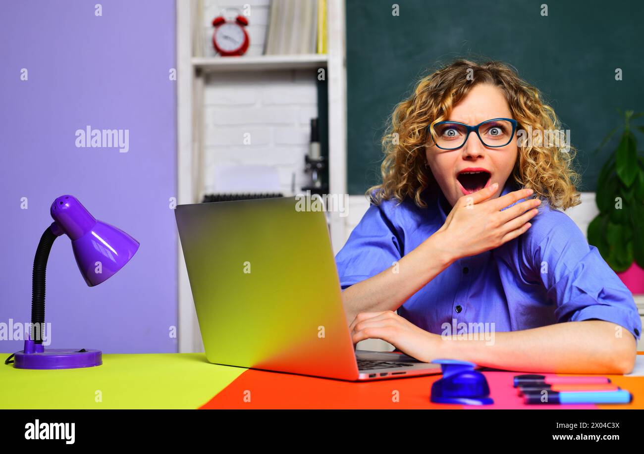 Enseignante surprise dans des lunettes assise au bureau travaillant avec un ordinateur portable en classe. Étudiante fille étudiant en ligne. E-learning au collège universitaire Banque D'Images