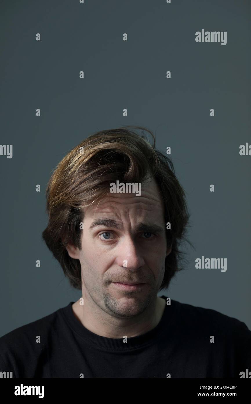 Portrait vertical avec fond gris d'un homme adulte aux cheveux bruns courts. Expression faciale drôle. Souriez. t-shirt noir yeux clairs Banque D'Images