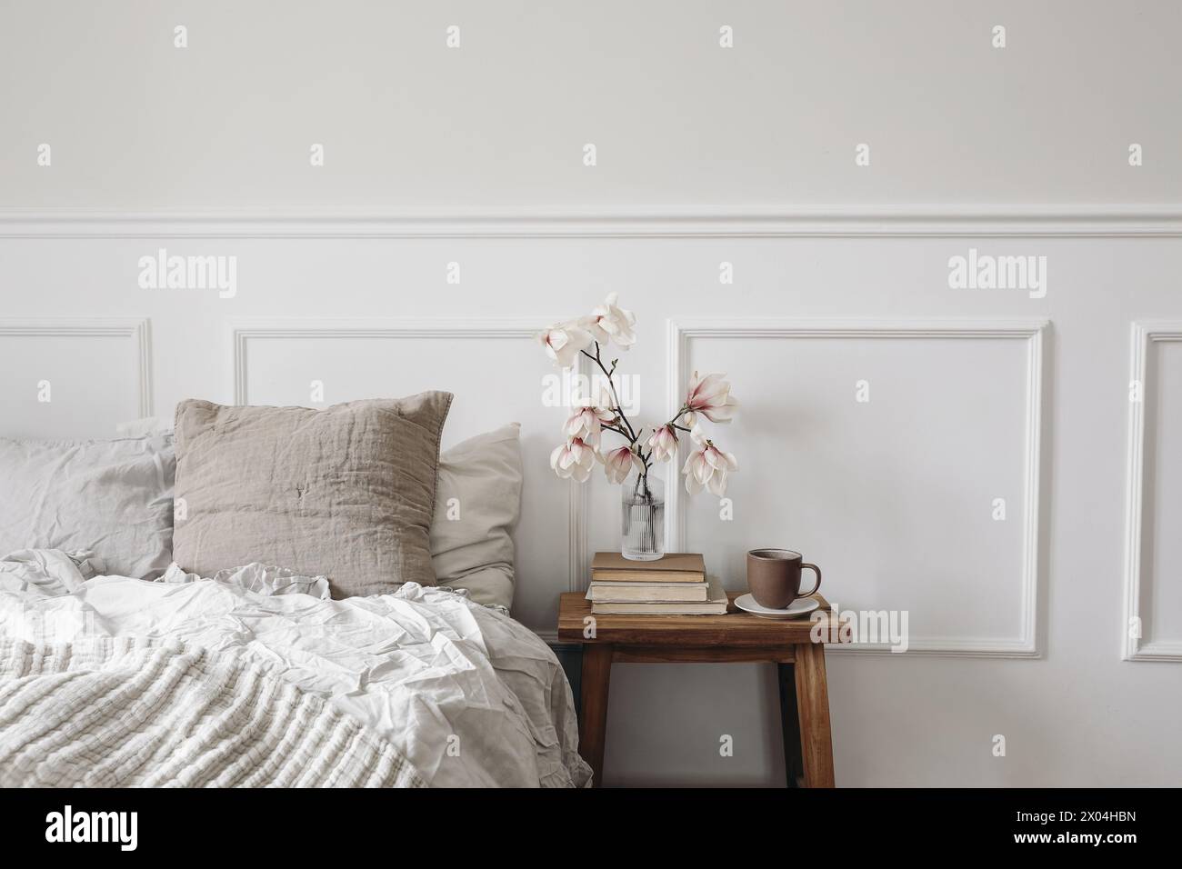 Chambre élégante. Table de nuit en bois avec vase en verre cannelé. Boolming des branches de magnolia. Tasse de café sur de vieux livres. Intérieur scandinave. Lin Banque D'Images