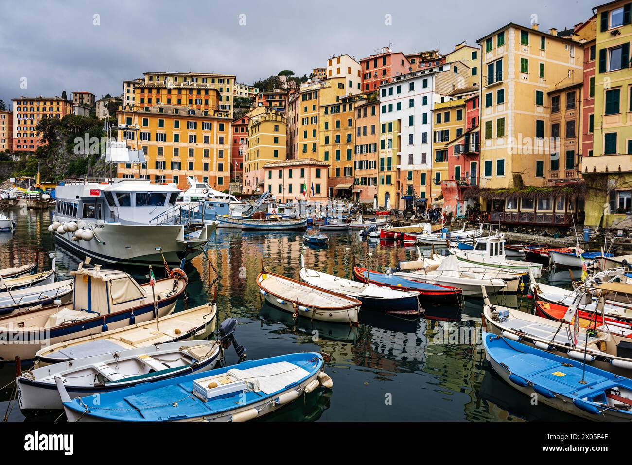 Bateaux de pêche dans le port de Camogli Italie reflétant dans l'eau avec les appartements anciens colorés au premier plan. Banque D'Images