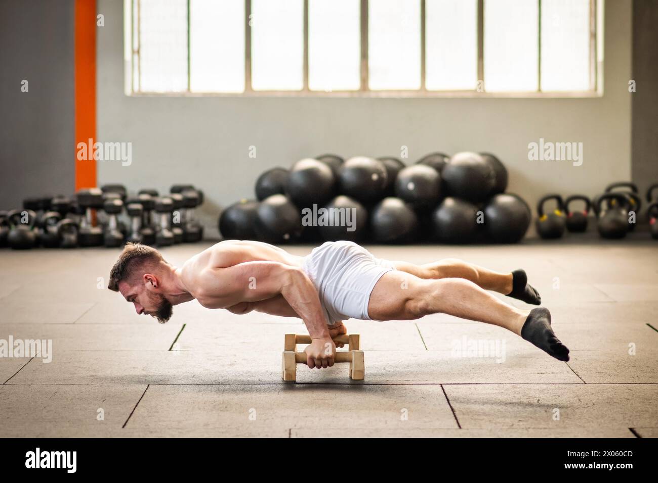 Corps entier de mâle musclé en short blanc avec poignée blocs étirant le corps tout en faisant face vers le bas pendant l'entraînement fonctionnel au centre de fitness Banque D'Images