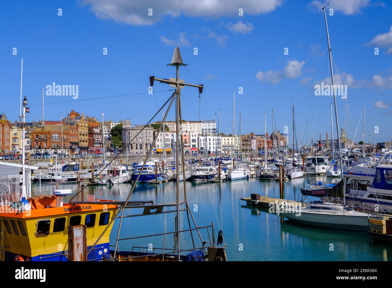 Ramsgate Royal Harbour rempli de divers bateaux et yachts, sous un ciel bleu avec des nuages blancs moelleux. Maisons en arrière-plan. Banque D'Images
