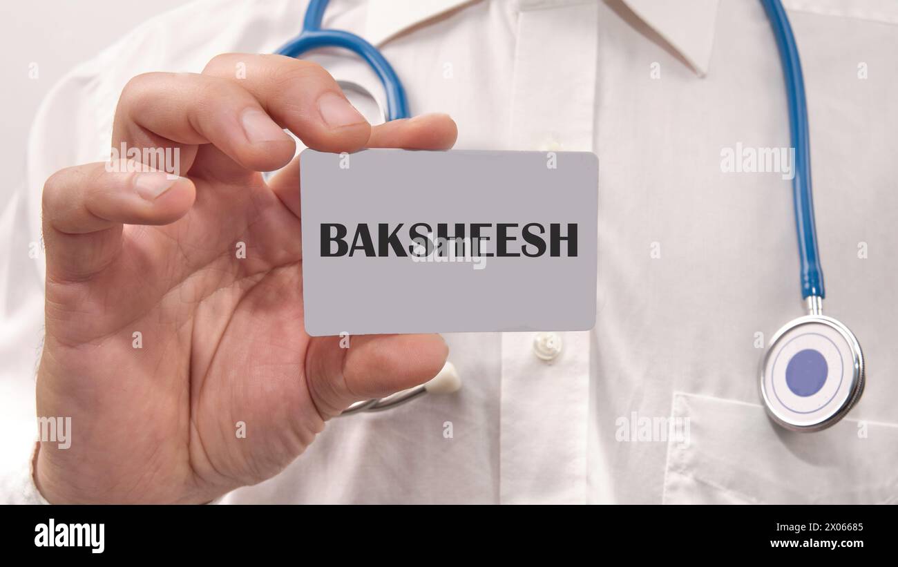 Mot BAKSHEESH écrit sur la carte dans la main d'un homme dans une chemise blanche Banque D'Images