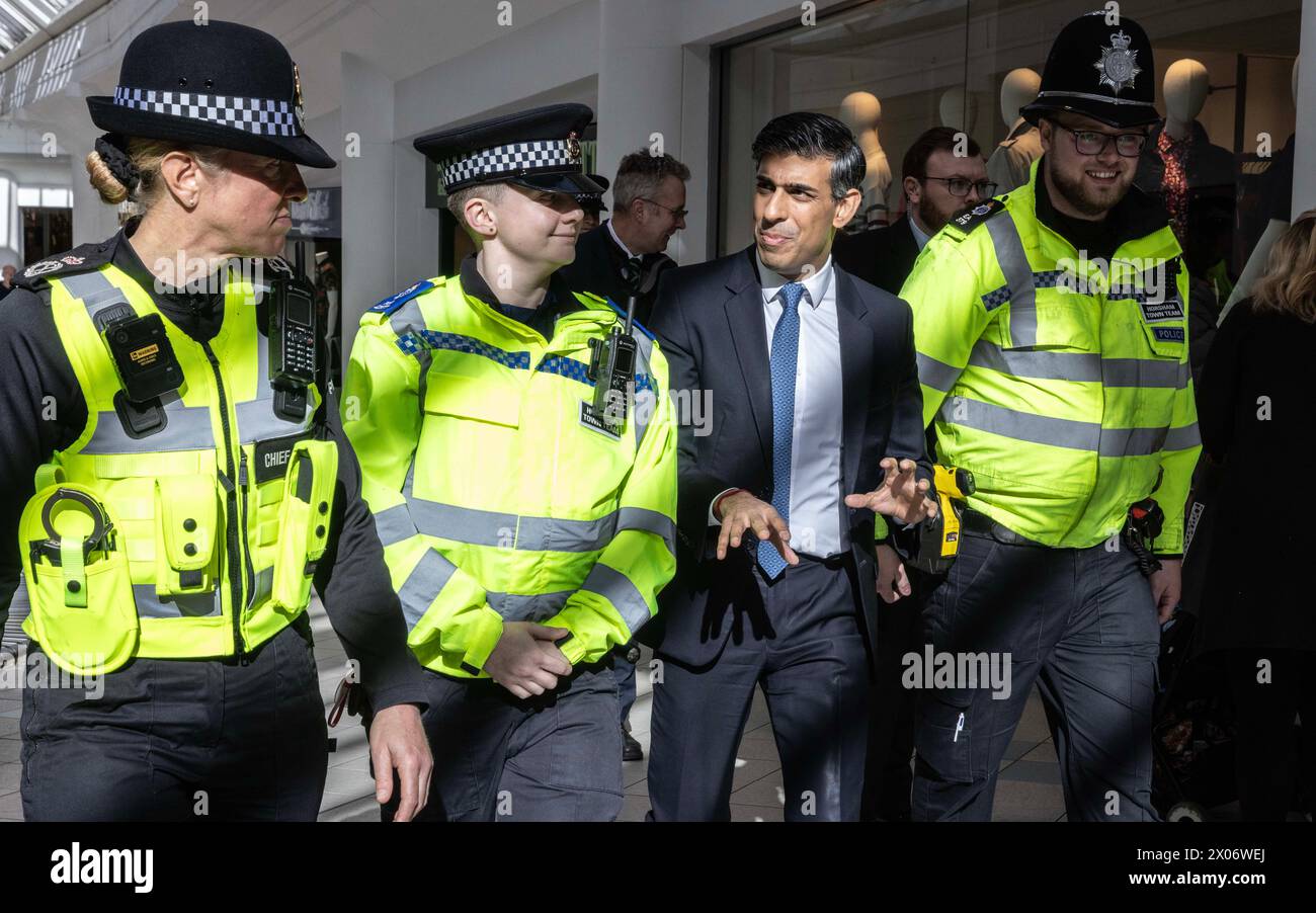 Le premier ministre Rishi Sunak traverse le centre commercial Swan Walk à Horsham, avec des policiers lors de sa visite dans le Sussex de l’Ouest. Date de la photo : mercredi 10 avril 2024. Banque D'Images