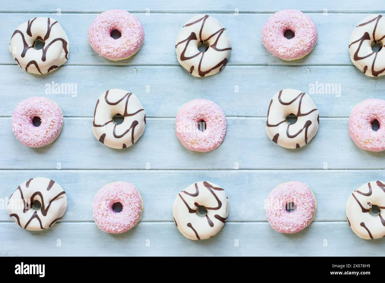 Aplatissement de beignets à la vanille givrés avec des tourbillons de chocolat et des beignets roses à la fraise avec des flocons de noix de coco. Vue du dessus de la table suspendue. Fond plat Banque D'Images