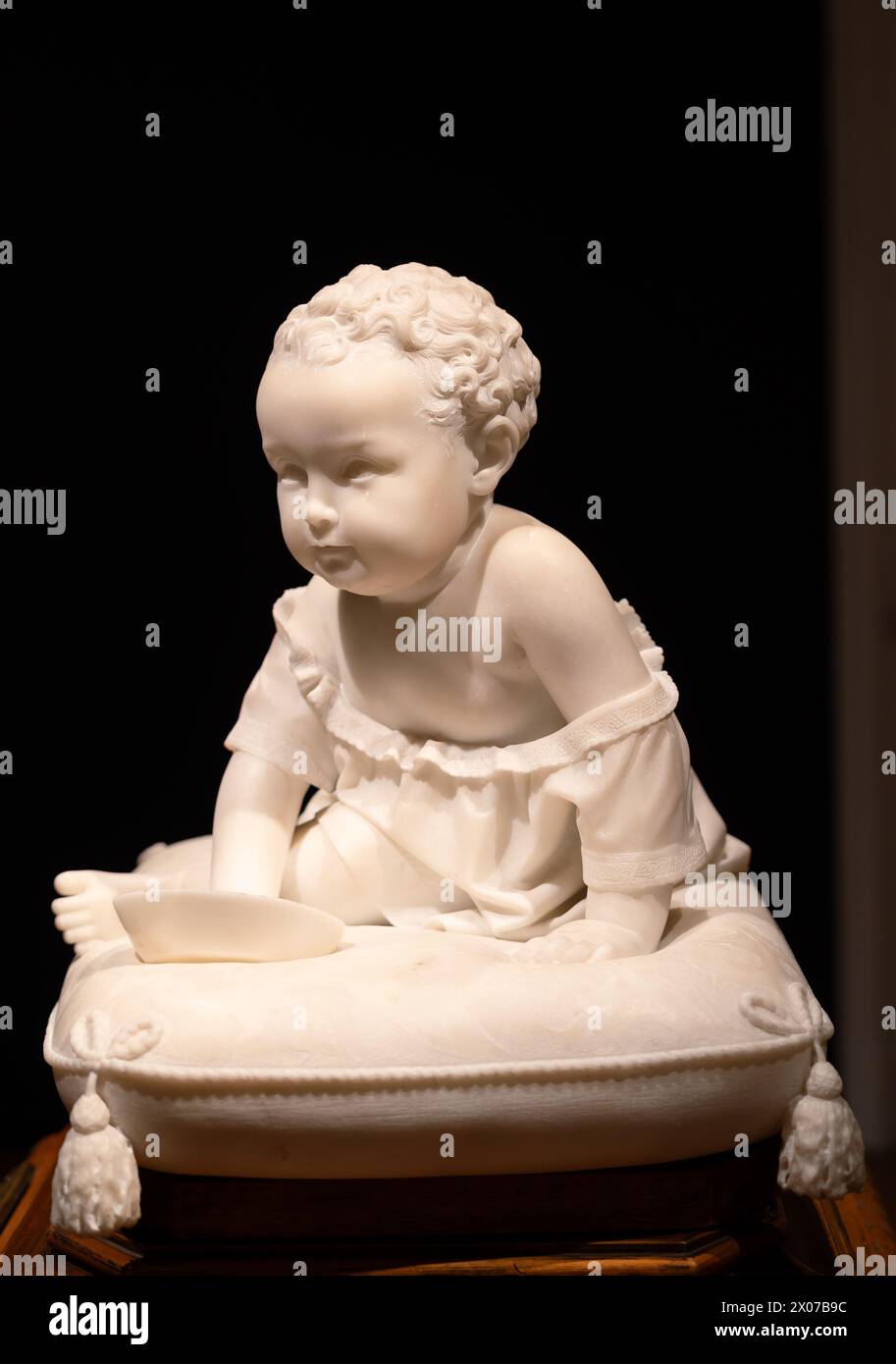 Statue en marbre de bébé garçon dans une robe assise sur un coussin Banque D'Images