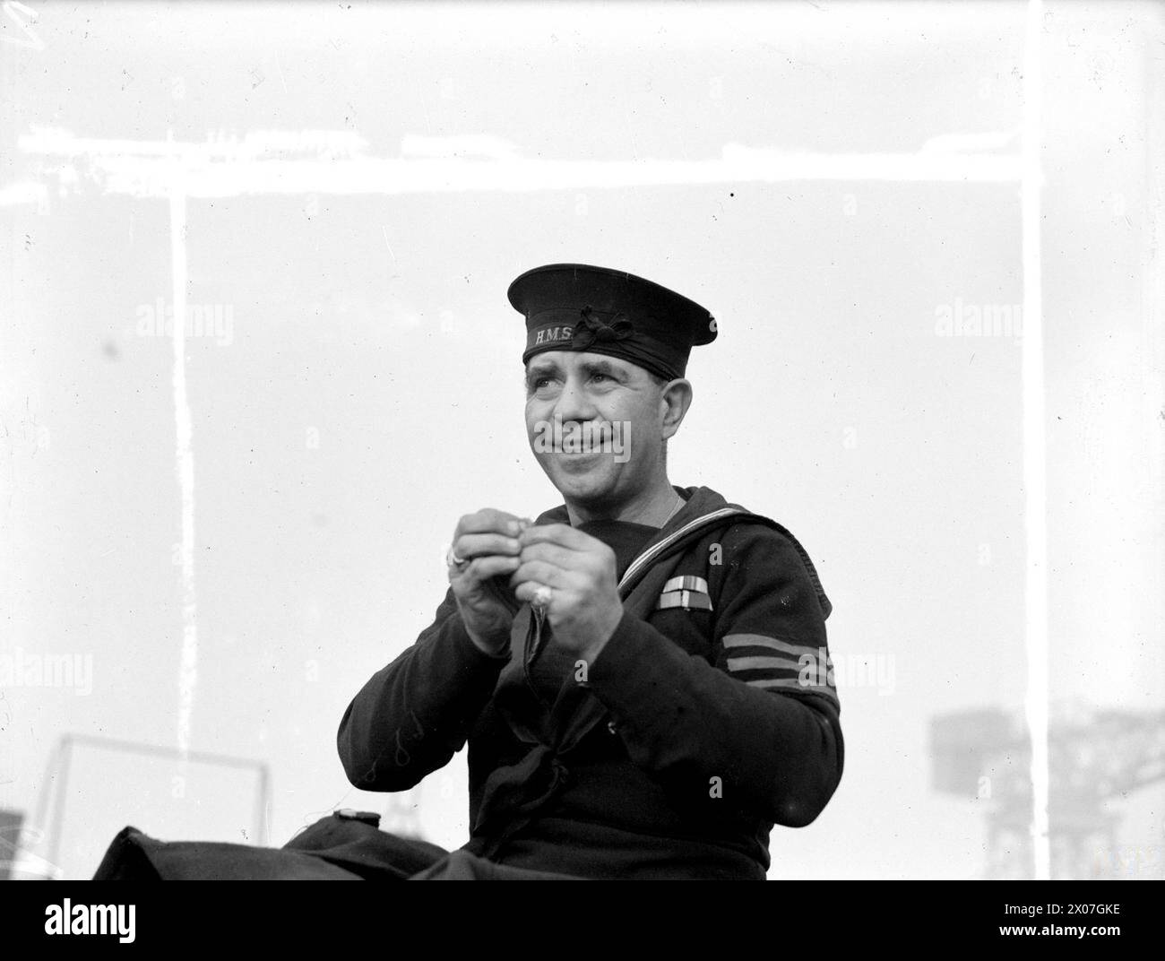 Le 13 décembre 1943 à Portsmouth, AB Henry Stewart Gunn, le plus ancien membre d'équipage du croiseur HMS Ajax avec 29 ans de service dans la Royal Navy, est montré enfilant une aiguille. Banque D'Images