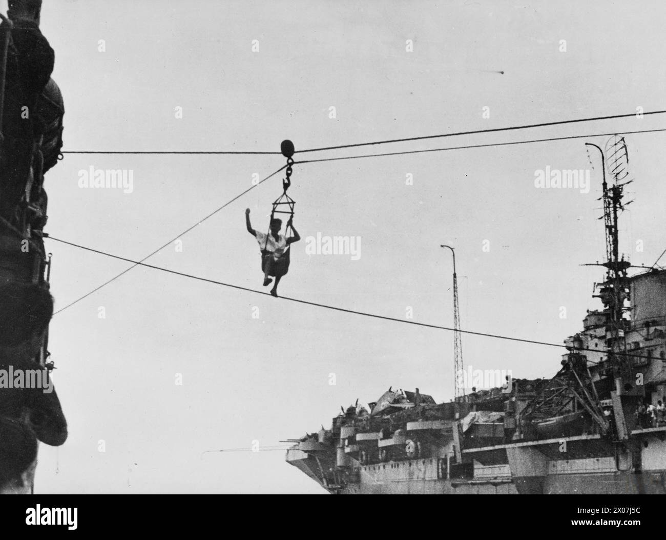 En juillet 1945, un navire militaire rejoint le HMS Kempenfelt, un destroyer britannique dans les eaux d'extrême-Orient, en étant transféré d'un porte-avions britannique dans une chaise suspendue. Il fit signe à ses collègues à bord du destroyer pendant le transfert. Banque D'Images