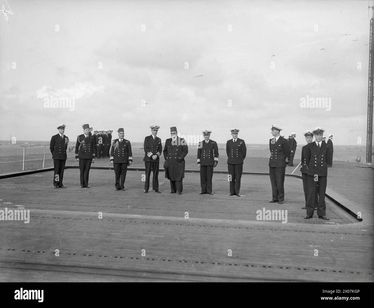 LE ROI FAROUK VISITE LE PORTE-AVIONS D'ESCORTE BRITANNIQUE. MARS 1945, À BORD DU HMS HUNTER, ALEXANDRIE, ÉGYPTE. - Le roi Farouk avec le vice-amiral Tennant et son état-major montant au pont d'envol du HUNTER au moyen de l'ascenseur de l'avion Banque D'Images
