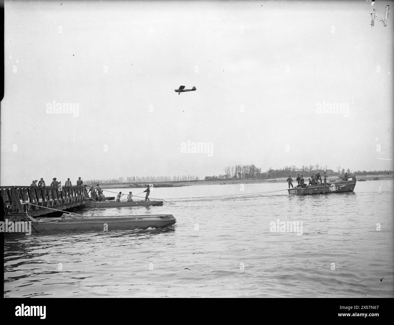 LA ROYAL NAVY PENDANT LA SECONDE GUERRE MONDIALE - Une embarcation de débarquement aidant à l'installation d'une section de pont après le remorquage de la banque. Un avion d'observation Taylorcraft Auster vole bas à mi-distance. Cette base avancée d'embarcations de débarquement mobiles de la Royal Navy, située à Reichswald, en Allemagne, joue un rôle important dans la traversée du Rhin par l'armée Banque D'Images