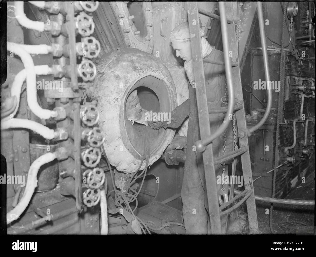 Un stoker à bord du HMS Curacoa à Rosyth passe une brosse de nettoyage à un compagnon à l’intérieur de la chaudière du croiseur pendant la seconde Guerre mondiale. Banque D'Images