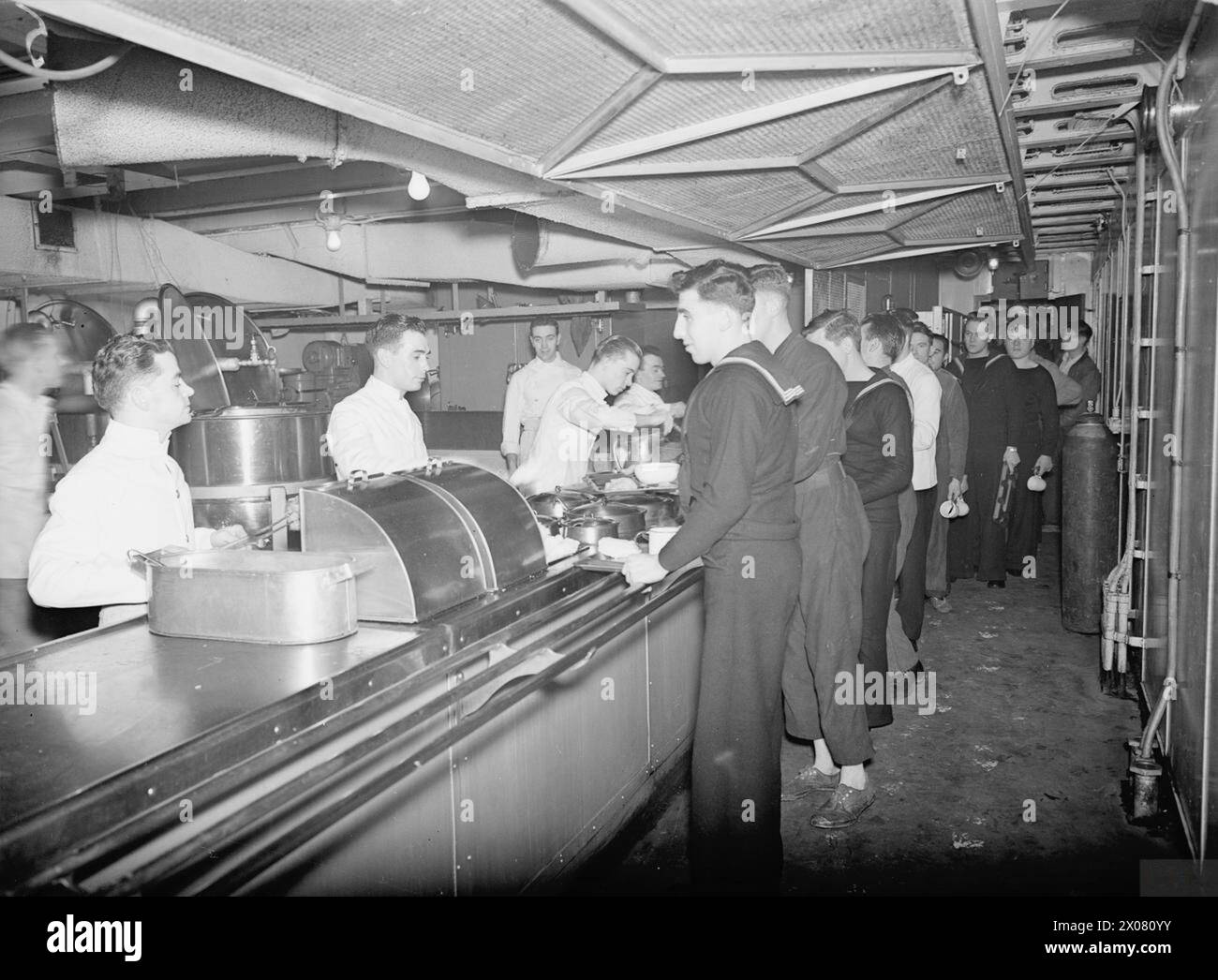 CAFÉTÉRIA MESSING : UNE EXPÉRIENCE À BORD D'UN NAVIRE DE GUERRE BRITANNIQUE. DÉCEMBRE 1942, LIVERPOOL, À BORD DU HMS DASHER. LE MESSING DE CAFÉTÉRIA EST ESSAYÉ COMME UNE EXPÉRIENCE DANS QUELQUES NAVIRES DE GUERRE BRITANNIQUES QUI ONT ÉTÉ ÉQUIPÉS OU RÉAMÉNAGÉS AUX ÉTATS-UNIS. - Marins servis avec dîner au comptoir de la cafétéria Banque D'Images