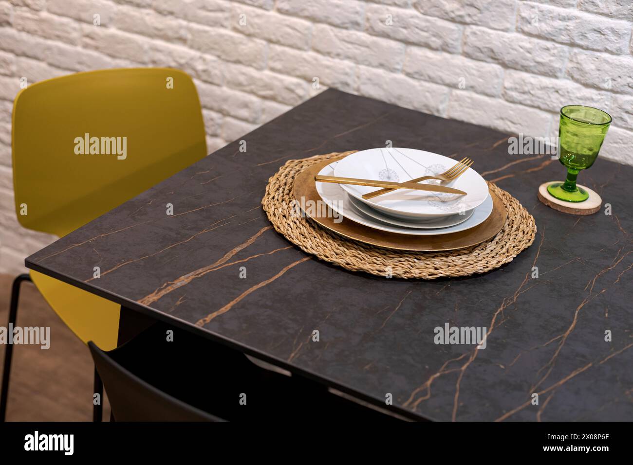 Table élégante avec assiettes blanches, couverts dorés et verre vert sur une table en marbre Banque D'Images