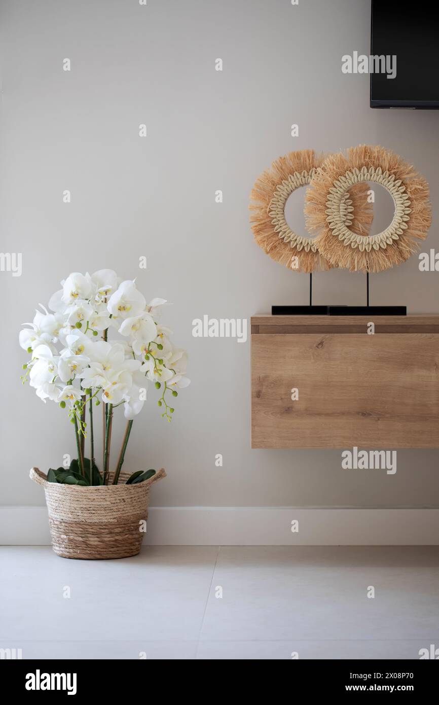 Design intérieur élégant avec une belle orchidée dans un panier tissé, avec deux décorations murales uniques et une console flottante en bois sous un plat-SC Banque D'Images