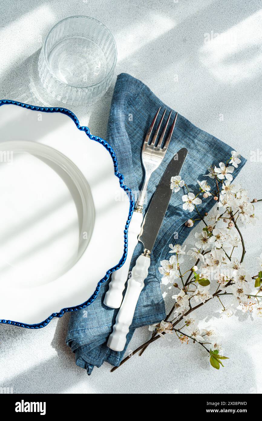 Une vue aérienne d'une table élégante qui comprend une assiette blanche avec un bord bleu, des couverts argentés, un verre, une serviette en denim et délicate cerise bl Banque D'Images