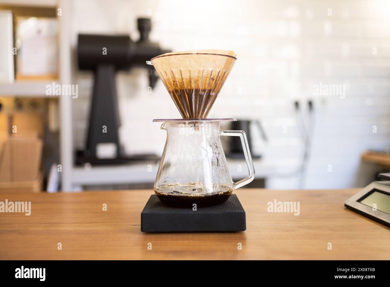 Une carafe à café en verre avec un filtre d'égouttement rempli de café moulu, réglée sur une balance numérique lors d'un processus de préparation manuelle dans un environnement de café moderne Banque D'Images