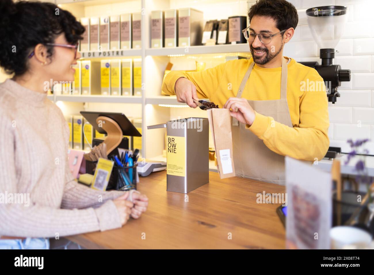 Homme hispanique joyeux barista servant un client dans un comptoir de café moderne. Banque D'Images
