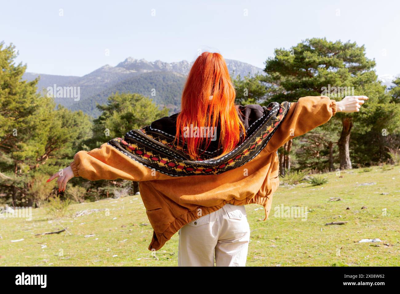 Vue arrière d'une femme rousse les bras tendus, embrassant la sérénité d'une scène de nature montagneuse, symbolisant la liberté et la paix Banque D'Images