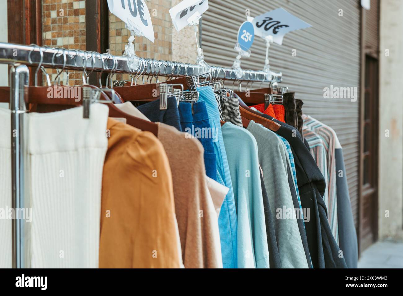 Une gamme d'articles de mode à prix réduit exposés sur un porte-vêtements à l'extérieur d'un magasin, avec des affiches de prix visibles attirant les acheteurs Banque D'Images