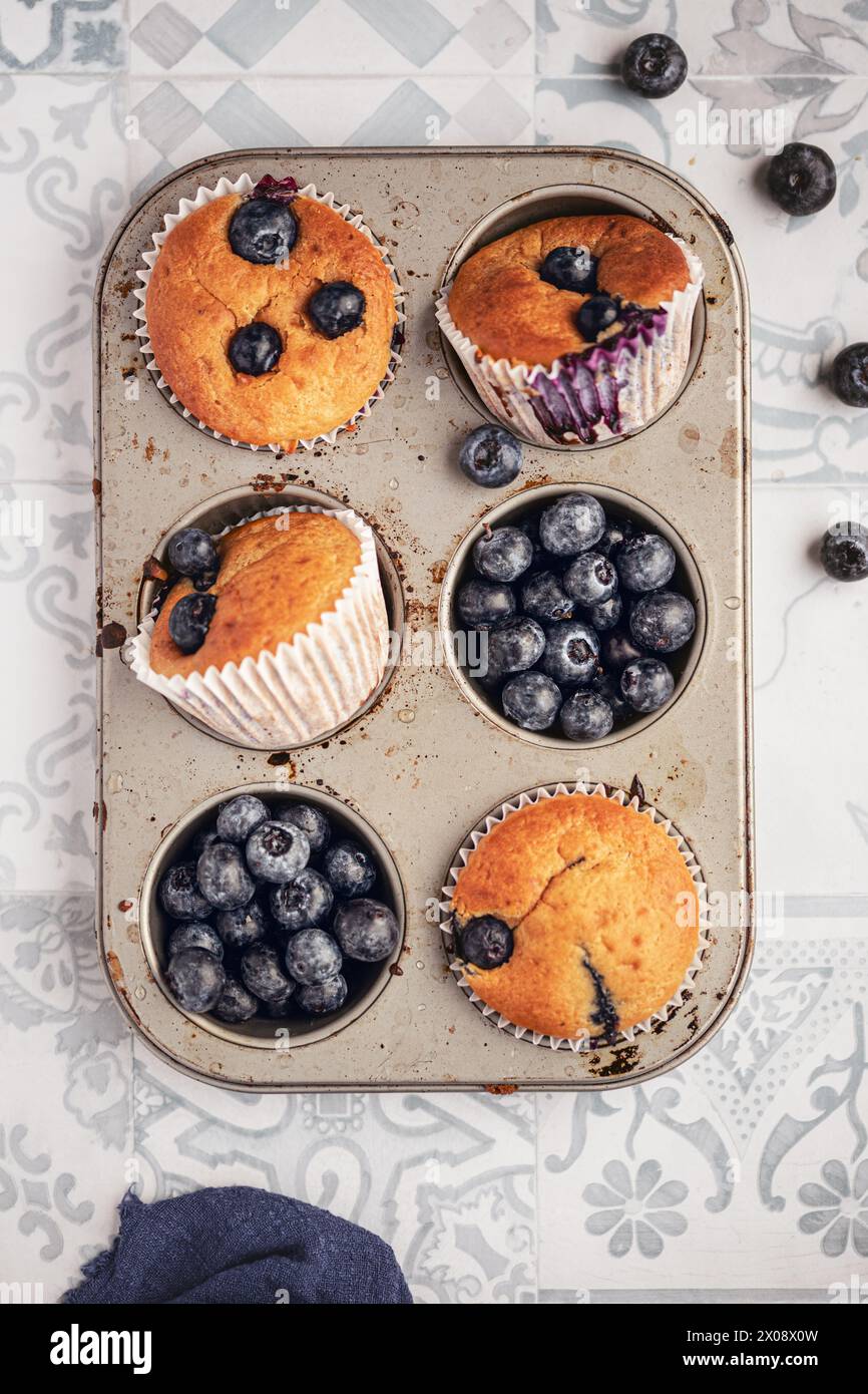 Une image appétissante montrant des muffins aux myrtilles fraîchement cuits et des myrtilles entières dans une boîte à muffins rustique Banque D'Images