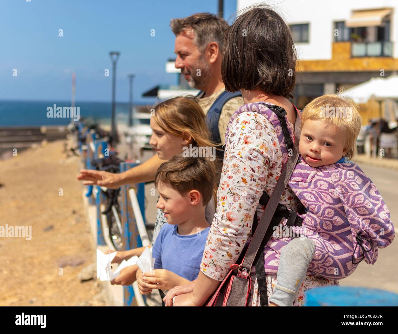 Une famille, avec une mère tenant un bébé garçon atteint du syndrome de Down, se tient aux côtés d'un père, d'une jeune fille et d'un garçon, tous engagés dans un moment partagé par le Banque D'Images