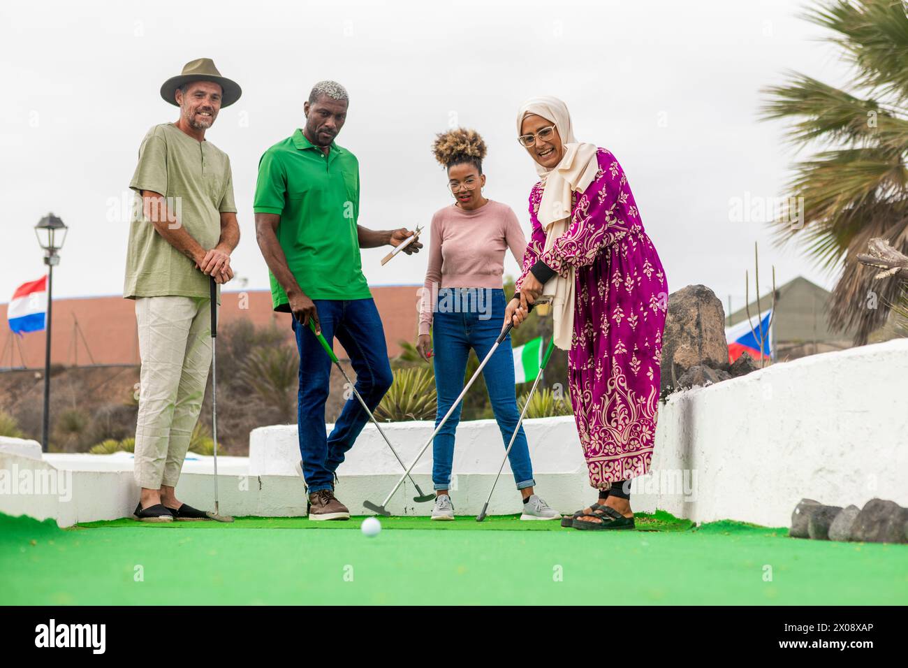 Un groupe de quatre amis divers est capturé ayant un moment agréable en jouant au mini-golf, avec des expressions d'engagement et de plaisir. Banque D'Images