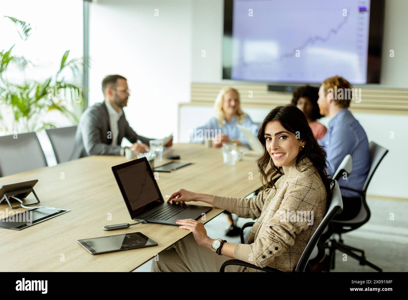 Femme d'affaires confiante s'engage dans une réunion, son sourire reflétant le succès et le travail d'équipe dans un cadre de bureau moderne. Banque D'Images