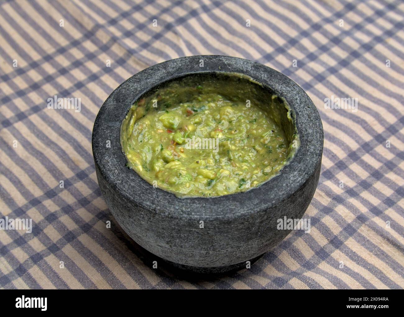 guacamole à l'intérieur molcajete (mortier mexicain traditionnel et pilon pour moudre les épices et faire des sauces) trempette d'avocat épicé avec des racines aztèques sur rayé Banque D'Images